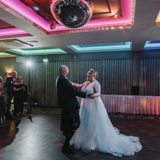 o	Bride and groom share first dance under colourful lights on dancefloor during last minute evening wedding reception in Scotland.