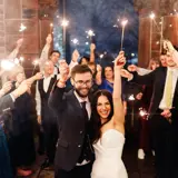 Couple holding sparklers with wedding party