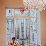 Couple posing infront of ornate window in hallway