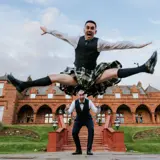 groom doing a funny split jump with best man peeking below him at boclair house