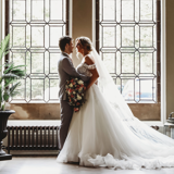 bride and groom standing inside ornate hall by window